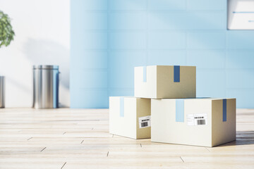 Poster - Cargo transportation service concept with cardboxes on light wooden floor in sunny office room with blue wall
