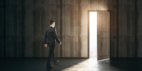 Wall Mural - Businessman walking towards exit in a dark concrete room. Leadership and future concept