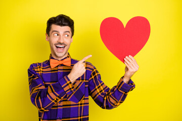 Poster - Photo of guy hold red paper heart card direct finger wear bow tie plaid shirt isolated yellow color background