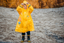 Boy In Yellow Raincoat On A Deserted Beach On A Cloudy Day