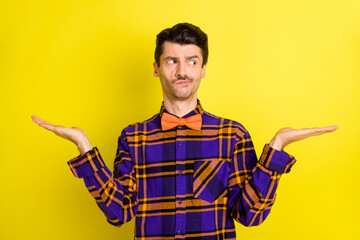 Wall Mural - Photo of young man unhappy uncertain look empty space hold two hands compare product advert isolated over yellow color background