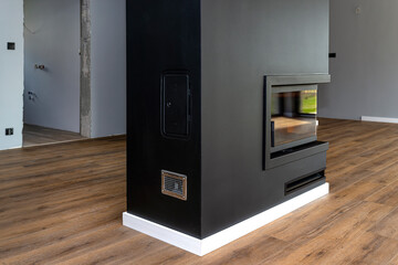 Wall Mural - A modern fireplace with a closed combustion chamber standing in the living room, painted black, with a corner pane covered with soot.