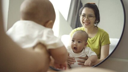 Wall Mural - Playful Asian mother and newborn baby boy having fun sitting looking at the mirror at home