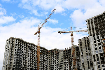 Wall Mural - Construction cranes above unfinished residential buildings on blue sky and white clouds background. Housing construction, apartment block in city