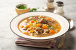 Beef and barley soup with celery, carrot and onion in plate on concrete background