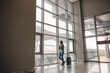 © Yaroslav Astakhov - Caucasian woman is standing alone near airport terminal panoramic windows with luggage
