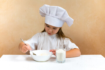 A little girl dressed as a cook kneads the dough. Cooking child lifestyle concept. The kid loves, has fun, studies and plays in the kitchen