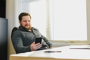 Wall Mural - Successful broker sitting and using smartphone in office.