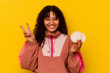 Wall Mural - Young mixed race sport woman holding a rice cakes isolated on yellow background showing number two with fingers.