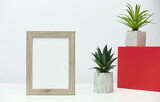 Fototapeta Sypialnia - Wooden vertical frame mockup with a plant and cactus in a concrete flowerpot on a white marble table and a red box.
