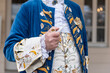 The details of man dressed in a baroque costume. A hand holding a pipe, golden buttons, vest and decorative hems.