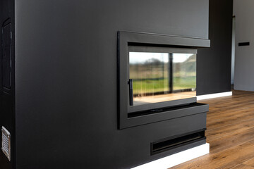 Wall Mural - A modern fireplace with a closed combustion chamber standing in the living room, painted black, with a washed corner pane.