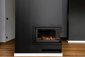 Wall Mural - A modern fireplace with a closed combustion chamber standing in the living room, painted black, with a washed corner pane.