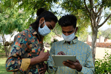 Sticker - Portrait of two young Indian friends in a medical face mask using a digital tablet in the park