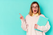 © Asier - Young student woman holding books isolated on blue background pointing to the side