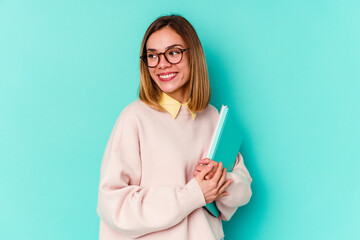 Young student woman holding books isolated on blue background looks aside smiling, cheerful and pleasant.