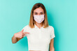 © Asier - Young woman wearing a mask for virus isolated on blue background person pointing by hand to a shirt copy space, proud and confident