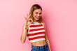 © Asier - Young caucasian woman isolated on pink background winks an eye and holds an okay gesture with hand.