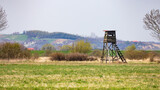 Fototapeta Krajobraz - Wooden hunting observation tower in the meadow. Photo taken at noon, soft light scattered by a thin layer of clouds.