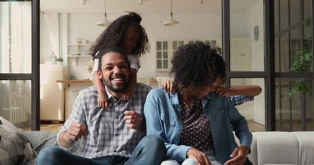 Wall Mural - Happy sincere young african american family couple parents laughing having fun with adorable little preschool son and daughter, playing together tickling on comfortable couch, enjoying leisure at home