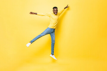 Wall Mural - Young happy energetic African man jumping with open arms and legs on isolated yellow studio background