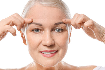 Wall Mural - Mature woman giving herself face massage on white background