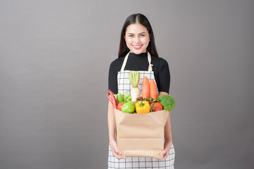 Portrait of beautiful young woman with vegetables in grocery bag in studio grey background