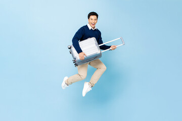Wall Mural - Jumping portrait of young happy smiling handsome Asian tourist man with baggage ready to travel isolated on light blue studio background