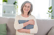 Photo of peaceful happy charming old woman hug embrace book reader sit couch indoors inside house home