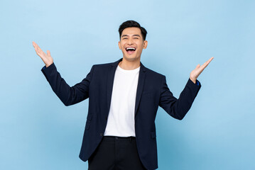 Surprised worry free handsome Asian man in semi formal clothes smiling and opening hands in light blue isolated studio background