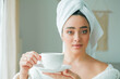 © Kristina89 - After a shower, a young woman in a bathrobe with a towel on her head drinks coffee and looks out the window. Morning. Breakfast. Cozy.