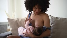 Black Mixed Mom Breastfeeding Cute Child Daughter On Couch Spbd. Calm Mother Sit On Couch With Child