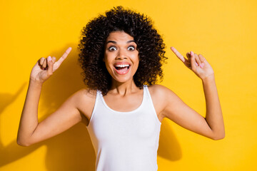 Poster - Photo of excited funny young dark skin woman dressed white tank-top pointing up empty space isolated yellow color background