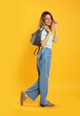 Canvas Print - Happy woman with backpack on yellow background