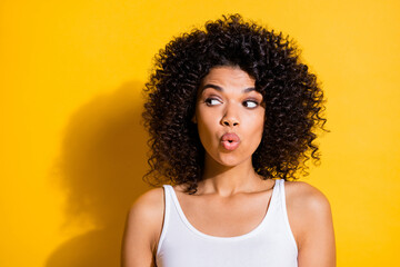 Wall Mural - Photo of pretty tricky young dark skin woman dressed white tank-top lips pouted looking empty space isolated yellow color background