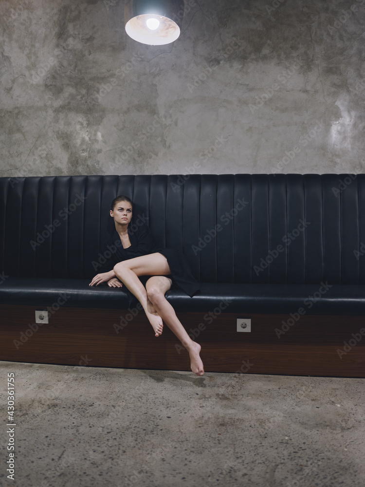 woman in dark clothes barefoot sitting on the sofa indoors lamp model interior - obrazy, fototapety, plakaty 