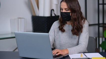 Wall Mural - Female employee stays in safety against viral diseases working in the office, woman wearing medical mask using the laptop indoor, protecting herself during pandemic. New social rules and distancing