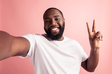 Wall Mural - Portrait of cheerful positive man take selfie show v-sign beaming smile on pink wall