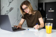 © dianagrytsku - Woman working on laptop at home on kitchen. writing on notepad. Business woman thinking about something important. Woman trying to find a job. Crysis. Girl styding from home