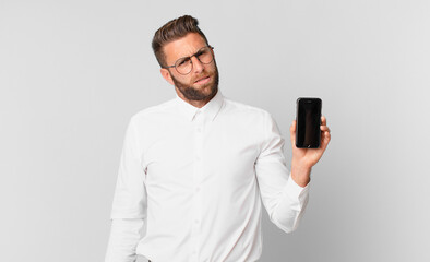 young handsome man feeling puzzled and confused and holding a cell