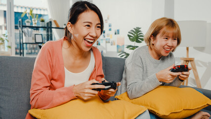 Sticker - Lesbian LGBTQ women couple play video game at home. Young Asia lady using wireless controller having funny happy moment together on sofa in living room. They have great and fun time celebrate holiday.