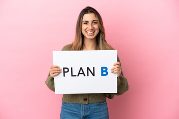 Sticker - Young caucasian woman isolated on pink background holding a placard with the message PLAN B with happy expression