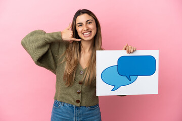 Wall Mural - Young caucasian woman isolated on pink background holding a placard with speech bubble icon and doing phone gesture