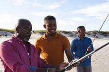 African American Father Teaching His Son How To Use Fishing Rods At The Beach