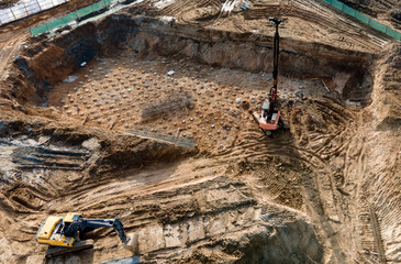 Poster - First floor slab rebar installation. Pile driver at construction site. Pile driven into ground by vibrating hydraulic hammer. Ground drilling machine. Drilling rig. Foundation pit for concrete pouring