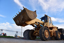 Wheel Loader With A Bucket At Construction. Heavy Machinery For Loading And Unloading Works And Road Work. Public Works, Civil Engineering, Road Construction. Tower Crane In Action. Crane On Formwork
