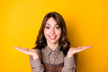 Poster - Photo portrait of girl keeping blank spaces on hands smiling isolated on bright yellow color background