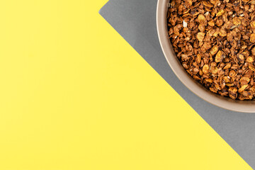 Wall Mural - Organic homemade roasted granola cereal with oats, flax, almonds, chocolate in round baking tray on yellow and gray background. Top view, flat lay muesli with copy space