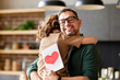 © JenkoAtaman - Little girl daughter congratulating dad with Fathers day or Birthday and giving him greeting postcard with red heart, happy man daddy embracing his child. Family holidays and celebration concept