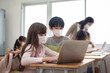 © eggeeggjiew - Diverse Multi Ethnic little girls and boys wearing protective face masks using laptop for studying in classroom at primary school